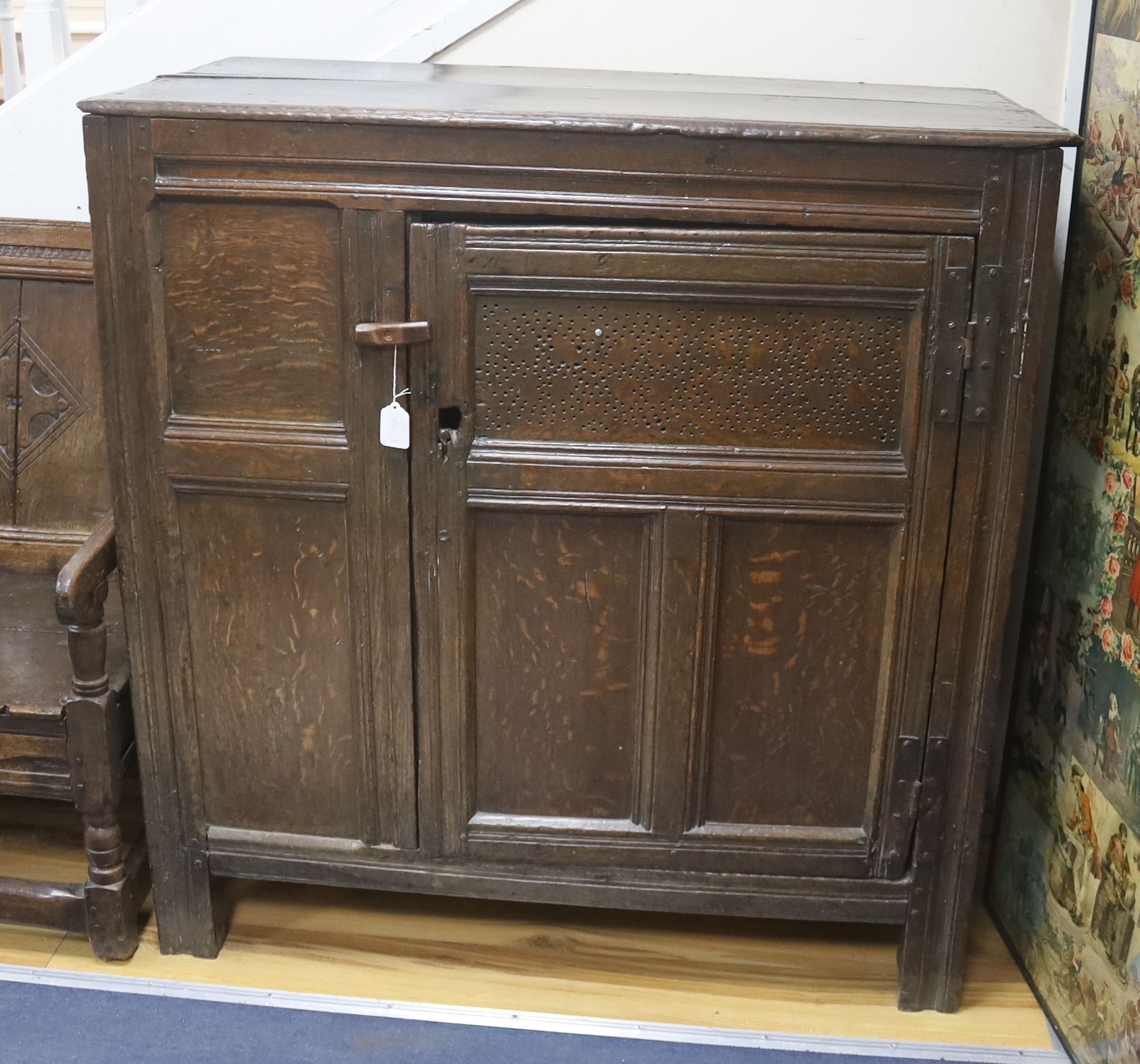 An early joined oak food cupboard, the planked top above a single hinged pierced panelled door, width 112cm, depth 55cm, height 115cm